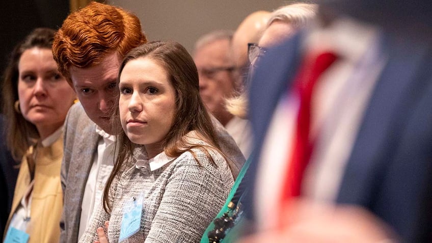 A man with red hair whispers to a woman.