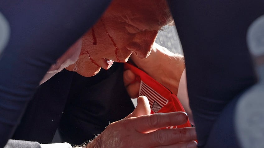 Donald Trump on the ground onstage at a rally with blood on his face
