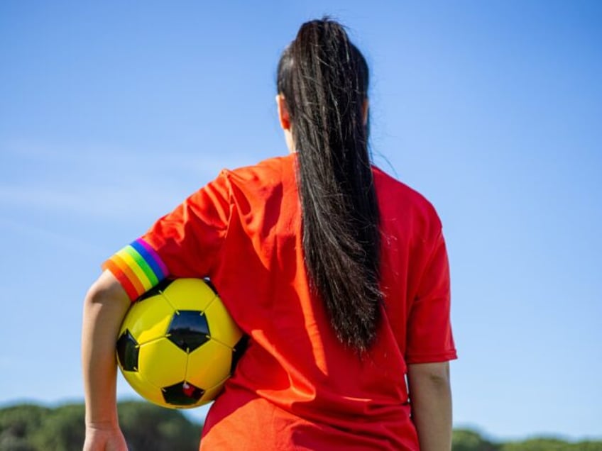 Soccer player woman with a soccer ball and captain armband with the LGBT pride flag on the