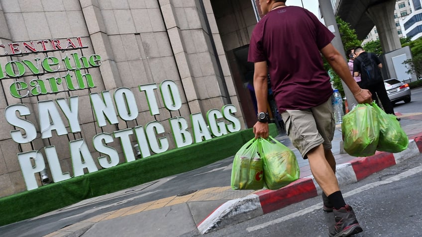 A man carrying goods in plastic bags crosses a street where a sign promoting a plastic bag-free shopping experience is displayed outside a department store. (Photo by ROMEO GACAD/AFP via Getty Images)