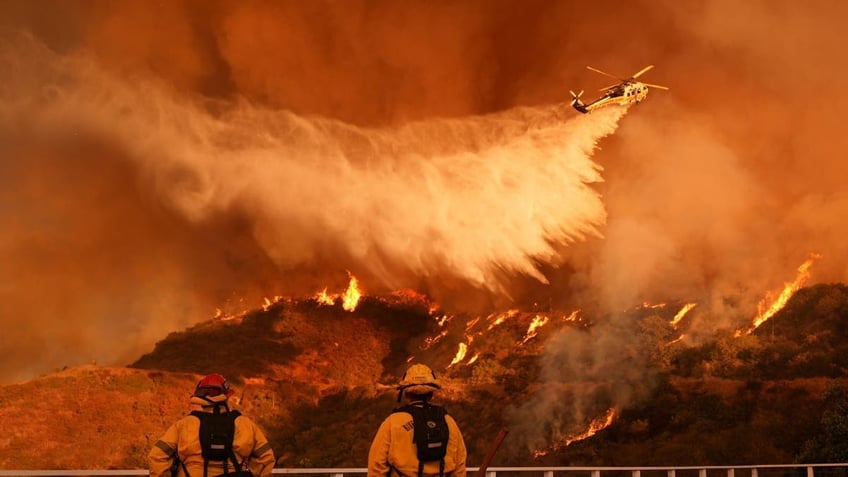 Firefighters watch a helicopter drop water on the Palisades Fire in Mandeville Canyon in Los Angeles, on Saturday, Jan. 11, 2025. (AP Photo/Jae C. Hong)