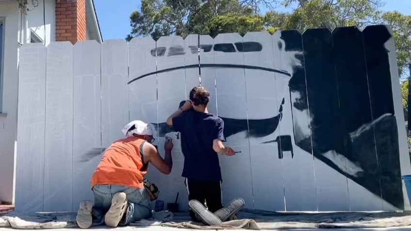 Wide image of artist painting boat mural