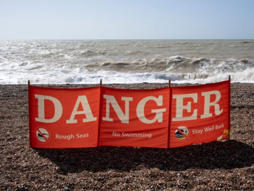 A seascape of a danger banner telling swimmers not to enter the water due to rough seas, o