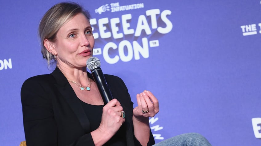 Cameron Diaz in a black blazer talks with her hands on stage 
