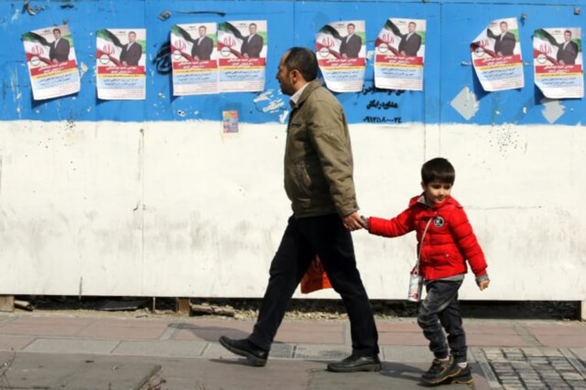 A man and a child walk past electoral campaign posters bearing portraits of a parliamentar