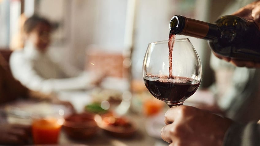 Close up of man pouring red wine into a glass in dining room.