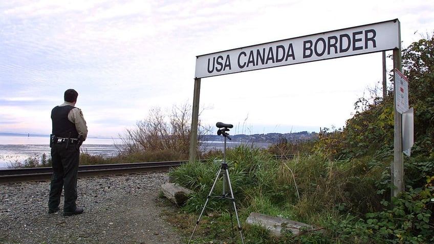 Canadian border officer looks to the border, sign to his right