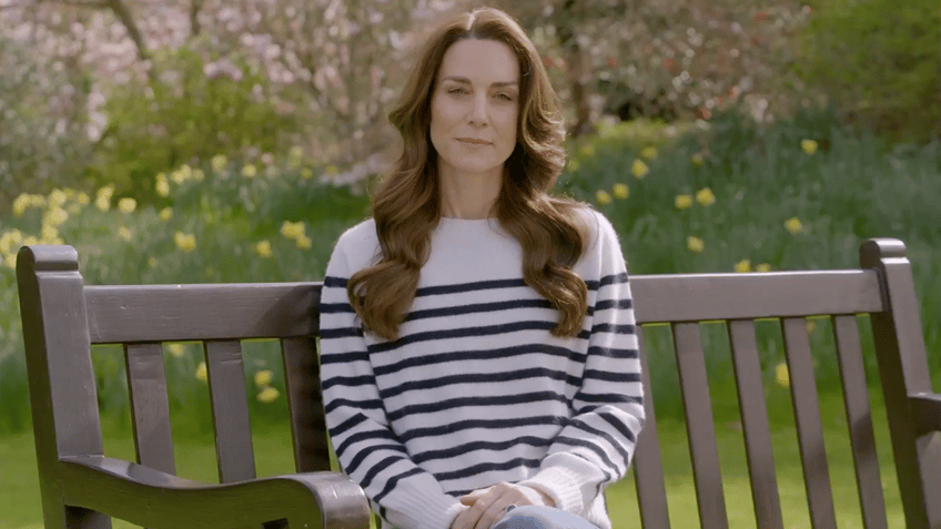 Kate Middleton in a white top with navy stripes sits on a bench to announce she has cancer