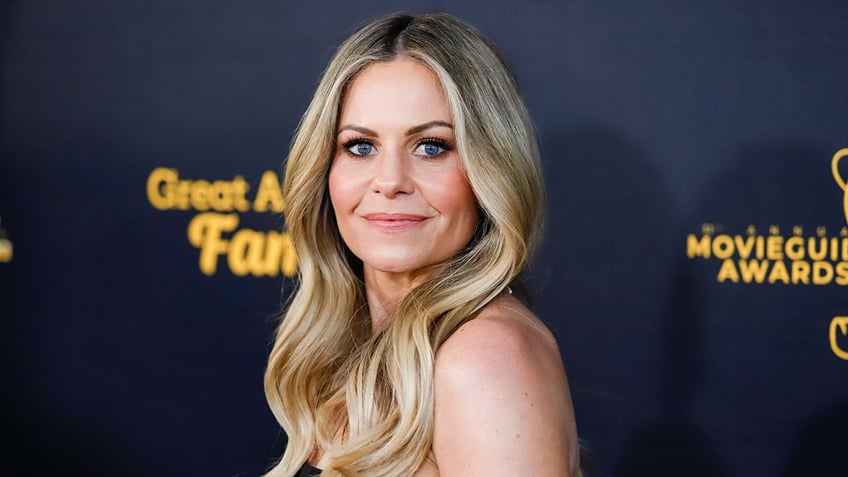 Candace Cameron Bure looks directly at the camera on the carpet, slightly over her shoulder