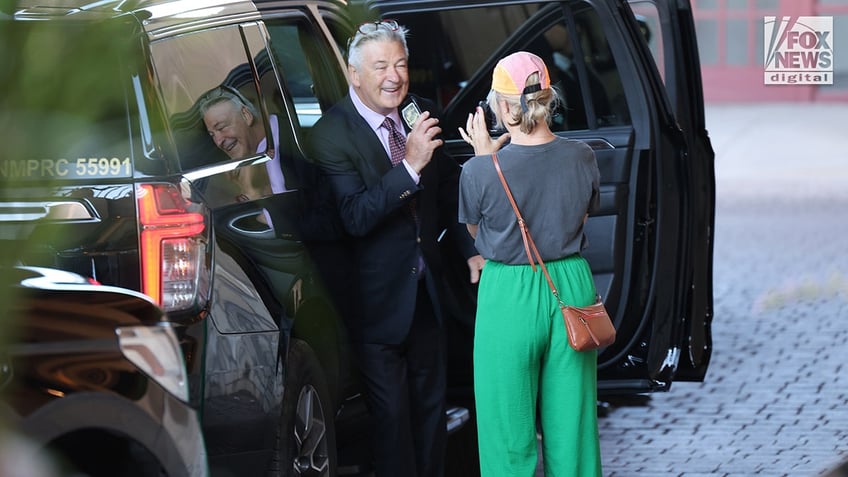 Filmmaker Jenna Rosher (R) films Alec Baldwin departing his hotel