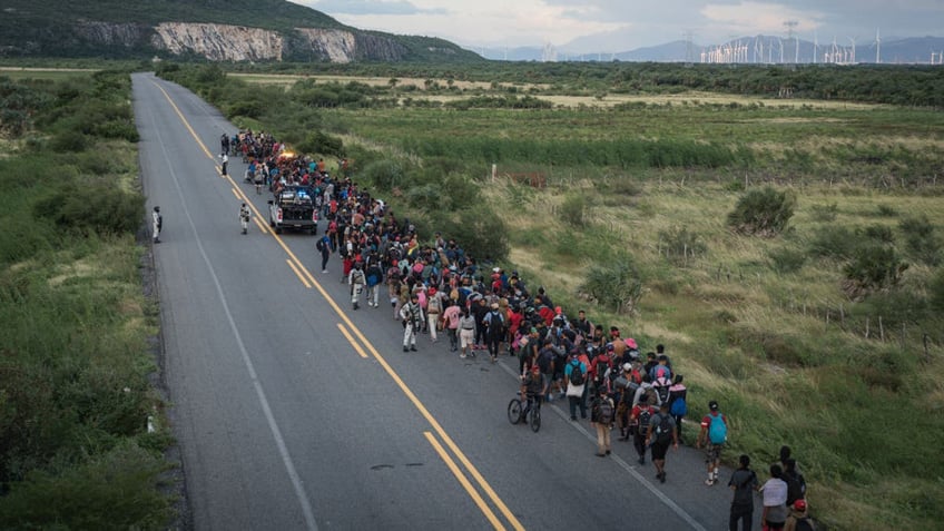 aerial shot of large group of migrants walking down desert road