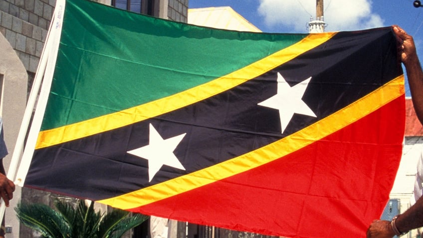 Two Men Holding St Kitts And Nevis Flag By Government Building