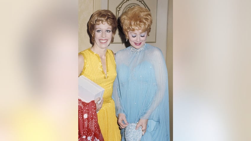Carol Burnett wearing a yellow dress next to Lucille Ball wearing a blue dress