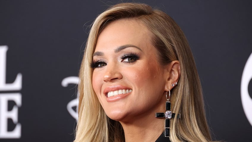 Carrie Underwood smiles wearing black cross earrings