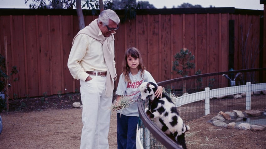 Cary Grant watching his daughter Jennifer as she holds a goat on a farm