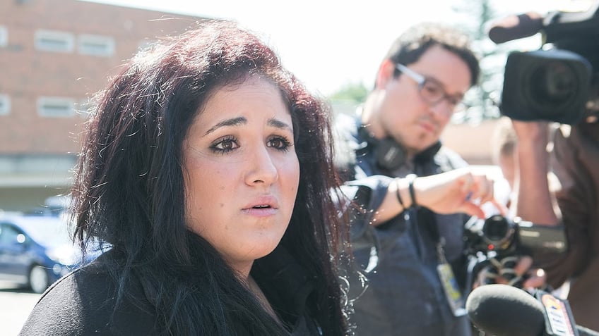 Liberty Kasem looking concerned in black as reporters photograph her.