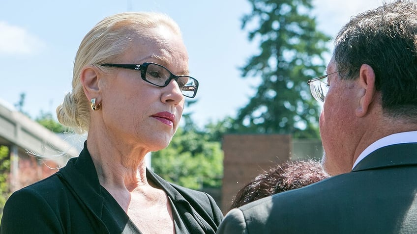 Jean Kasem wearing a black suit and glasses looking downcast.