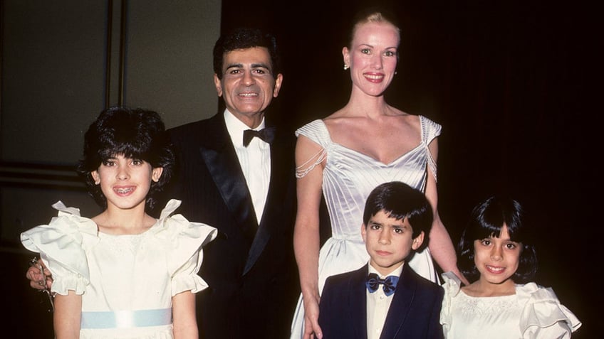 Casey Kasem in a suit and bow tie with Jean Kasem in a white dress posing with his three children.