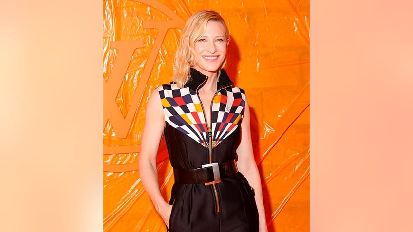 Cate Blanchett in a black printed shirt with white, orange and red squares and a large belt on the carpet