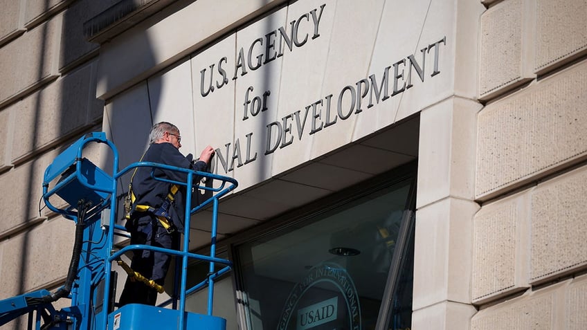  A worker removes the U.S. Agency for International Development sign on their headquarters on February 07, 2025 in Washington, DC. 