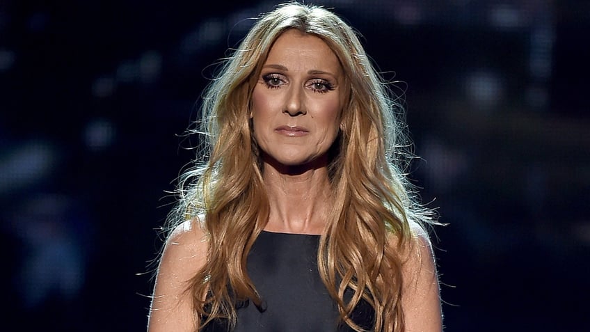 Celine Dion stands on stage wearing black dress