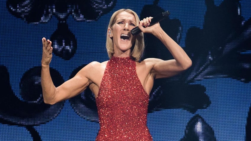 Celine Dion in a halter red sparkly dress sings passionately into a microphone as she holds it above her