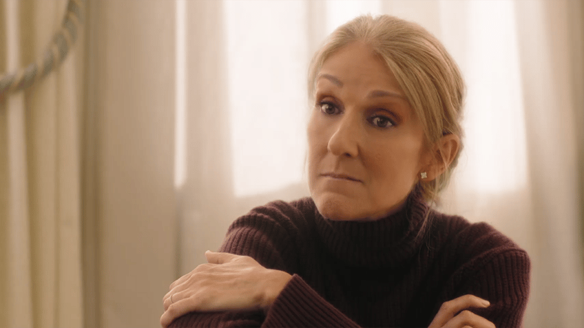 Celine Dion has her arms crossed and looks slightly perplexed in the film "Love Again"