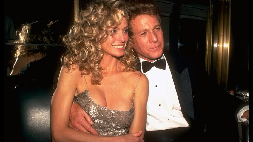 Farrah Fawcett in a sparkly dress cuddling up next to Ryan ONeal in a suit and bowtie