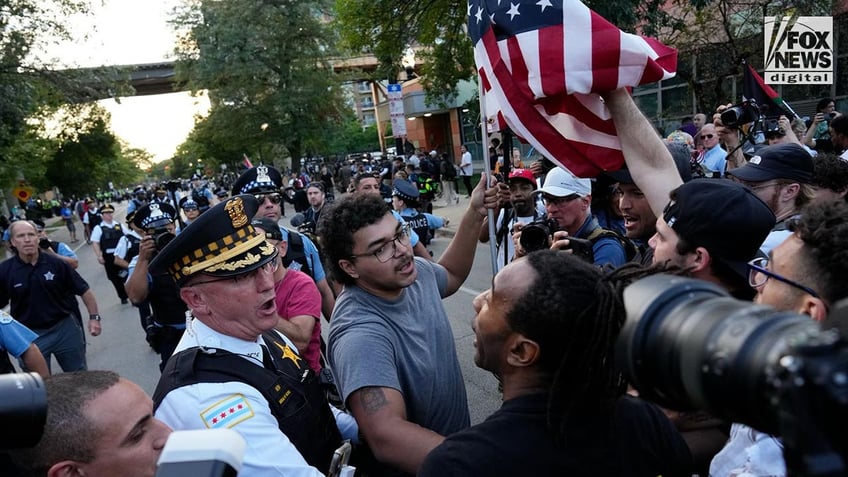 A man with an American flag is yelled at by protestors as he is removed by police in Chicago during a march on the DNC