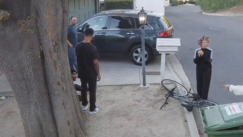 Brian J. White stands next to a tree and a man sitting on the ground in security footage