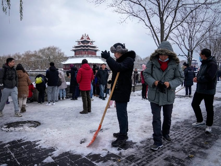 City workers clear the snow on a pathway as people take pictures of the snow covered Turret of the Forbidden City in Beijing, Monday, Dec. 11, 2023. An overnight snowfall across much of northern China prompted road closures and the suspension of classes and train service on Monday. (AP Photo/Andy Wong)