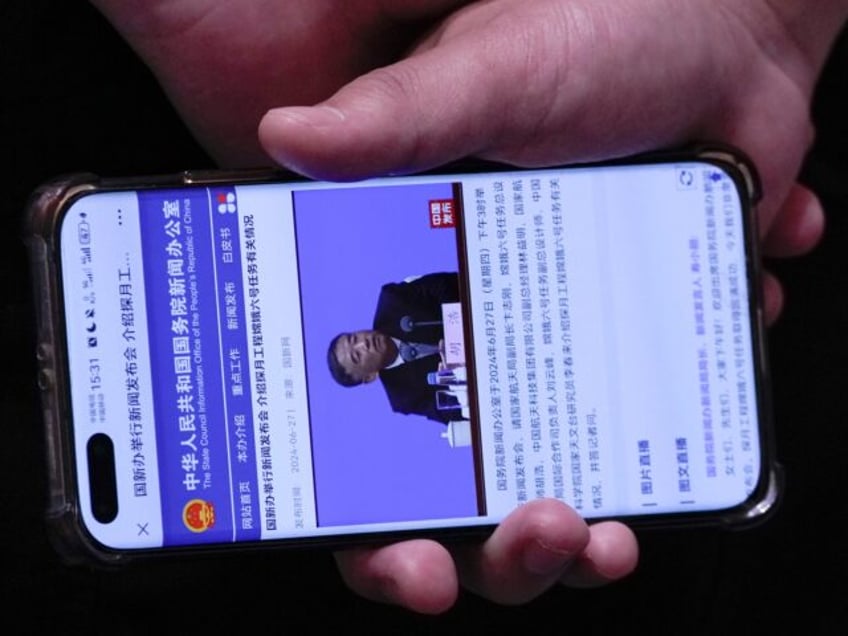 A staff member holding a smartphone showing the State Council Information Office website b