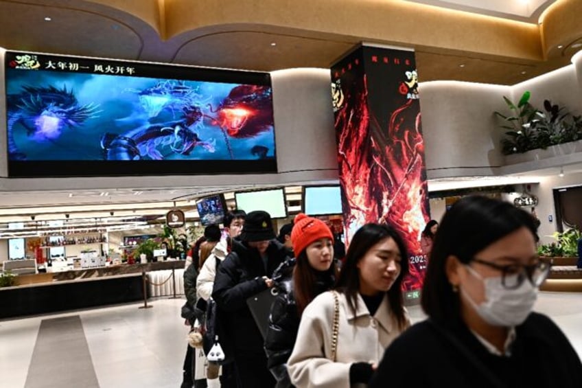 People queue as a screen shows scenes from the animated film 'Ne Zha 2' at a movie theatre