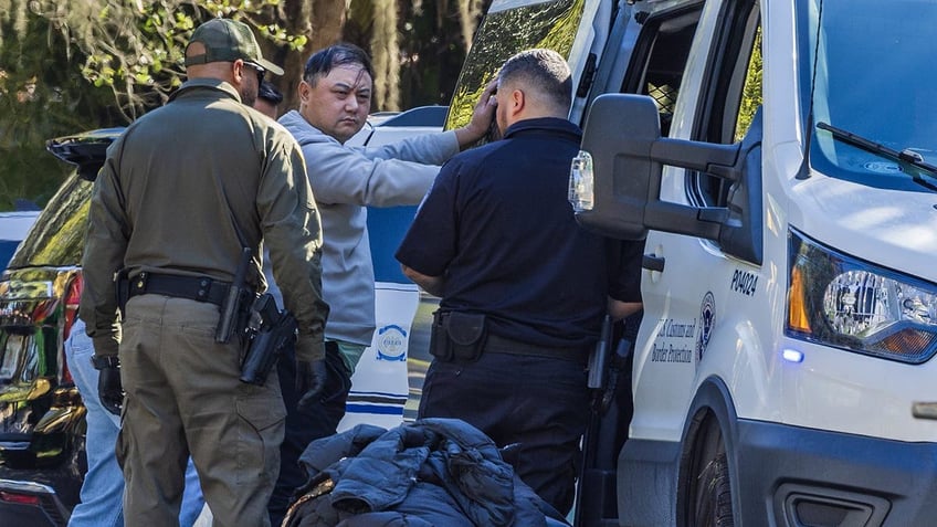 Authorities process a man who has his hands on the side of a van