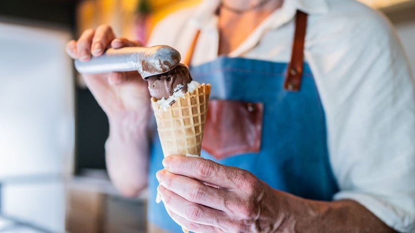 Man scooping a chocolate scoop on top of a vanilla scoop.