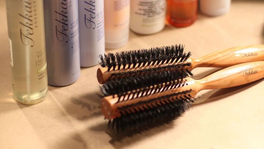 Round hairbrushes sit on a table in front of hair products