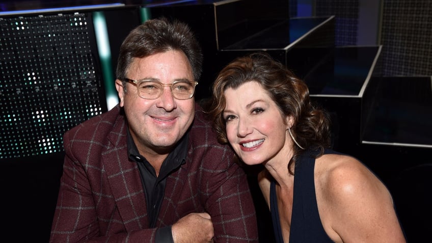 Vince Gill in a burgundy plaid suit with Amy Grant leaning on him, wearing a black dress