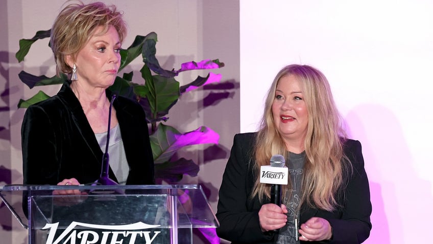 Christina Applegate sits on stage with a microphone opposite Jean Smart