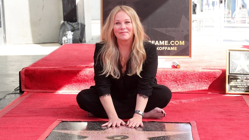 Christina Applegate places her hands on her star on the Walk of Fame as she sits on the ground