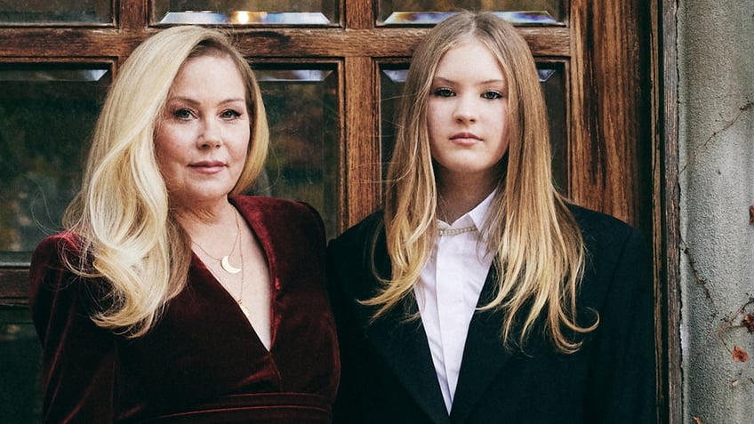 Christina Applegate in a red dress standing next to her daughter in front of their home.