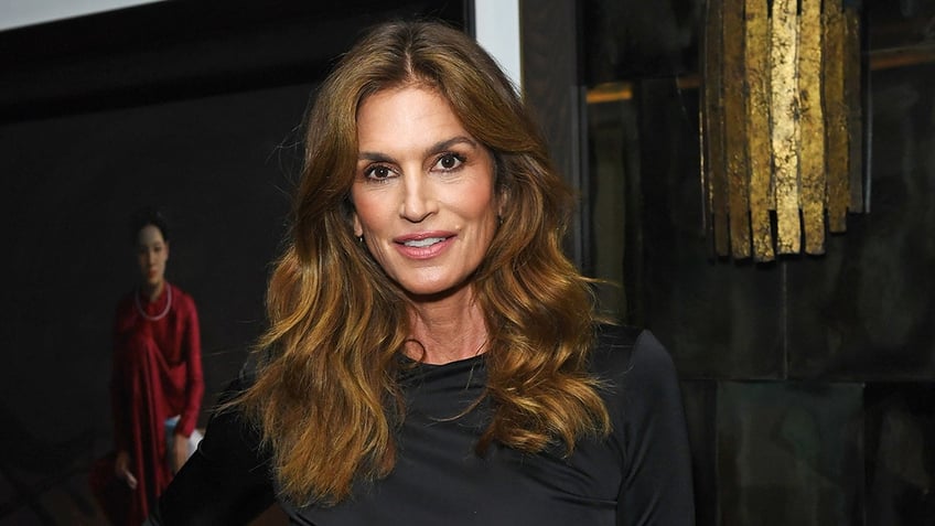 Cindy Crawford with brown wavy hair in a black outfits smiles for the camera