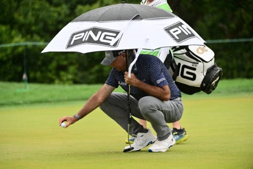 Former British Open winner Stewart Cink places his ball on the eighth green while under an