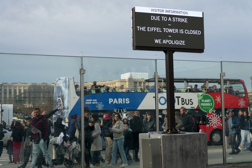 This photograph taken on December 27, 2023 in Paris shows tourists behind a board informing visitors that the Eiffel Tower is closed after staff went on strike. The strike on the 100th anniversary of the death of engineer Gustave Eiffel, who built the tower, was to protest about "the current way it is managed", the hard-left CGT union said in a statement. (Photo by Dimitar DILKOFF / AFP) (Photo by DIMITAR DILKOFF/AFP via Getty Images)