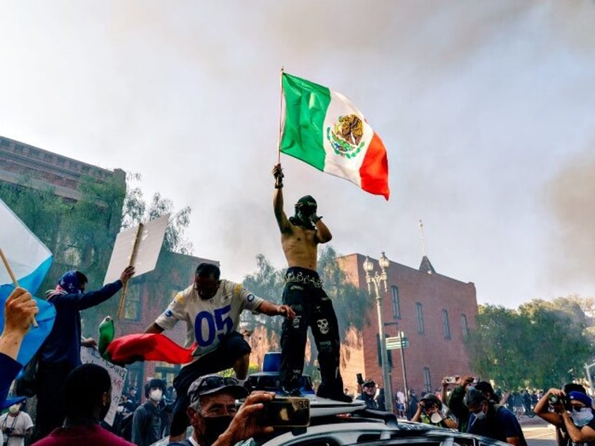 Protesters stand on top of a destroyed vehicle in Los Angeles, California, US, on Sunday,