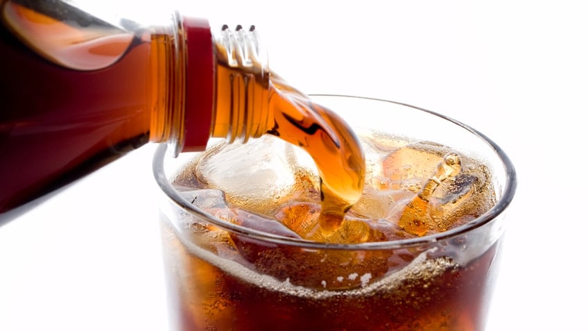 A soda is poured into a glass with ice.