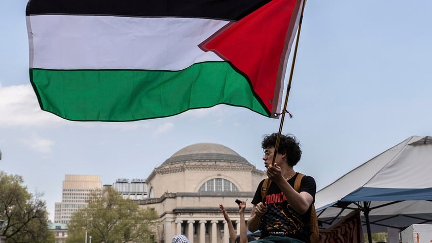 A student protester waves a large Palestinian flag at their encampment on the Columbia University campus