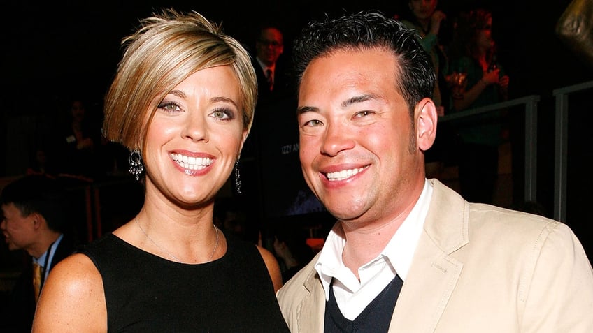 Kate Gosselin in a black dress with a choppy short haircut smiles next to Jon Gosselin in a tan blazer and dark sweater