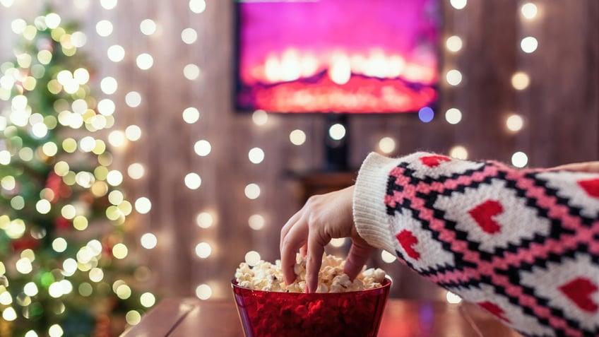 A hand reaching for popcorn as a holiday movie plays