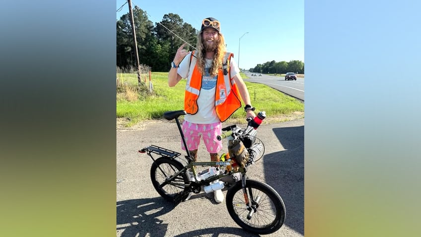 US comedian Sebastian 'Seabass' Fowler posing behind his BMX beside a highway, smiling at the camera