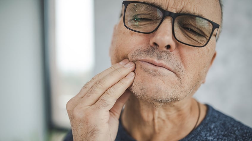 male holding his cheek in pain, experiencing tooth ache